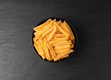 Kızarmış cips çubukları siyah kasede, parmak patates cipsi, altın ayakkabı teli patates kızartması, patates kızartması, patates kızartması, kızarmış patates, koyu taş masa arkasında patates.