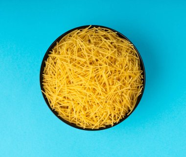 Mavi arka planda çiğ vermicelli, yuvarlak altın çorbalı makarna, küçük ev yapımı erişte, ince makarna, siyah kasede sarı filini makarna.