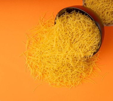 Turuncu arka planda çiğ vermicelli, yuvarlak altın çorba makarna, dağınık ev yapımı erişte, ince makarna, siyah kasede İtalyan sarısı filini makarna.