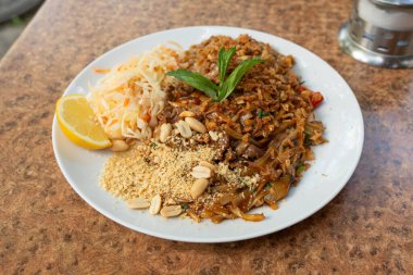Pad Thai veya Phad tha Asya eriştesi yakından. Çin pirinçli makarna, etli Tayland yemeği, erişte, taze lahana salatası ve bulanık arka planda sokak restoranında yeşillikler.