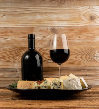 Peynir tabağı çeşitliliği, sarı, beyaz ve mavi gorgonzola tabağı kırmızı şarap bardağı, peynir tahtası, çeşitli doğranmış süt ürünleri, ahşap üzerinde kokulu Fransız peyniri.