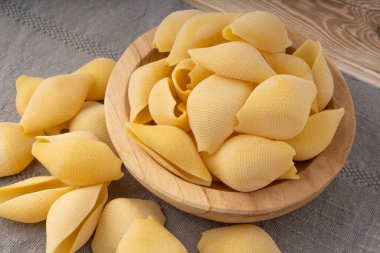 Tahta kasede çiğ konchiglionili makarna. Kuru, kabuklu şehriye, büyük İtalyan makarnası, beyaz arka planda buğday makarna.