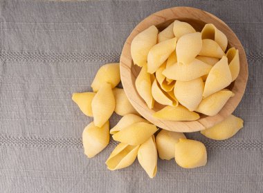 Tahta kasede çiğ konchiglionili makarna. Kuru, kabuklu şehriye, büyük İtalyan makarnası, beyaz arka planda buğday makarna.