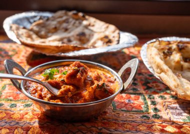 Tereyağlı paneer masala, peynirli Hint körisi peynir kübü, baharatlı tavuk korması, domates kremi soslu geleneksel yemek, geleneksel tekstil kaplı masa üzerindeki metal tabak.