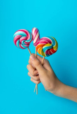 Elinde renkli lolipop, çubukta sarmal şeker, renkli çizgili lolipop, yuvarlak meyve şekeri, çok renkli şekerleme, mavi arka planda daire şeklinde lolipop, metin için kopyalama alanı