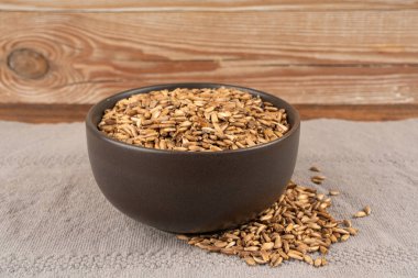 Süt tohumu yığını, silybum marianum tanecikleri, kuru mübarek süt devedikeni meyveleri, gri arka planda çeşitli devedikeni çekirdekleri, siyah kase, doğal organik şifalı bitkiler.