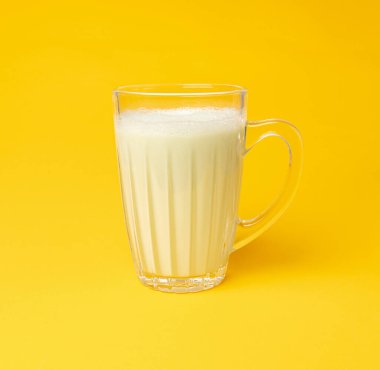 Bardakta vanilyalı milkshake. Sarı arka planda milkshake, beyaz süt proteini, meyvelerle harmanlanmış sağlıklı badem sütü.