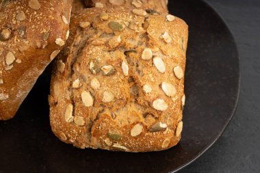 Kabak çekirdeği ekmeği yakın, makro kahvaltı ruloları ve pepita tohumları. Fitness karesi çöreği, sağlıklı burger, kabak tohumlu çörek ve siyah arka plan.