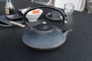 Japon çaydanlığı, siyah metal çaydanlık, çay için geleneksel demir çaydanlık sushi siparişini beklerken bambu çubuklarıyla turşulu zencefil ve wasabi turşulu restoran masasında bekliyor.