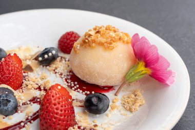 Meyveli mochi pirinç keki, beyaz daifuku, Japon geleneksel tatlısı, kremalı ve anko dolgulu yuvarlak wagashi, çilekli Asya şekeri, yaban mersini ve siyah arka planda çiçek.