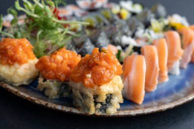 Baharatlı somonla kaplı çıtır tempura suşi ruloları taze mikroçerezler, çeşitli maki ruloları ve suşi tabağında yenilebilir çiçekler.