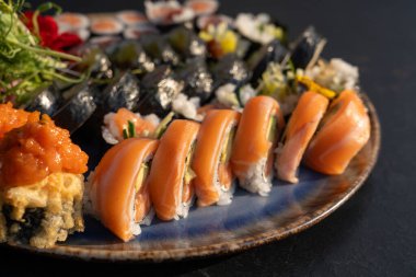 Somon, ton balığı, salatalık, avokado, yosun, pirinç, tempura sosu, mikroyeşillikler ve yenilebilir çiçeklerle çeşitli börekler. Japon yemek sunumunu seramik tabakta kapat