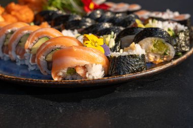 Somon, ton balığı, salatalık, avokado, yosun, pirinç, tempura sosu, mikroyeşillikler ve yenilebilir çiçeklerle çeşitli börekler. Japon yemek sunumunu seramik tabakta kapat