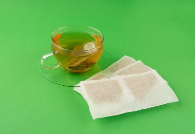 Fincanda bitki çayı kesesi, papatya çayı ve hiperikum ile sıcak su veya St. John 's Wort çay poşeti, tedavi amaçlı tıbbi içecek kupası, yeşil arka planda çay poşeti demleme süreci.