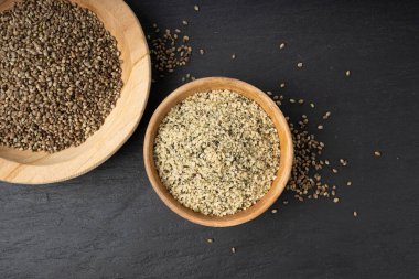 Kabuklu kenevir tohumları ahşap kasede, soyulmuş kenevir taneleri, kabuksuz marihuana çekirdekleri, siyah arka plan görünümlü yağ protein keneviri çekirdekleri