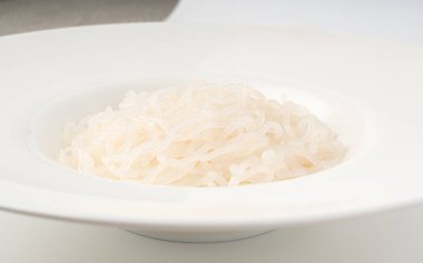 Shirataki ya da konnyaku makarna dokusu beyaz tabakta. Konjak jöleli erişte, Japon sıfır kalorili sirataki spagettisi, vegan cam vermicelli, geleneksel düşük kalorili yemek.