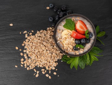 Siyah kasede pişirilmiş. Muzlu yulaf ezmesi sütlü yulaf lapası, çilek ve yabanmersini haşlanmış emmer, sağlıklı tahıl gevreği. Koyu arkaplanda taze yeşil naneli buğday taneleri.