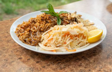 Pad Thai veya Phad tha Asya eriştesi yakından. Çin pirinçli makarna, etli Tayland yemeği, erişte, taze lahana salatası ve bulanık arka planda sokak restoranında yeşillikler.