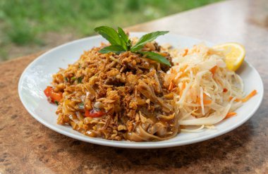 Pad Thai veya Phad tha Asya eriştesi yakından. Çin pirinçli makarna, etli Tayland yemeği, erişte, taze lahana salatası ve bulanık arka planda sokak restoranında yeşillikler.