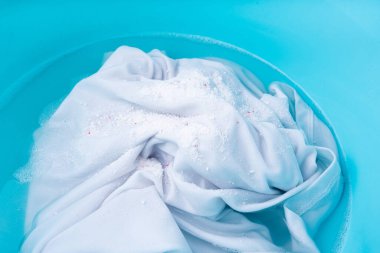 Çamaşırları mavi plastik bir leğende çamaşır deterjanı ve oksijen ağartıcı ile yıkamak, ıslak beyaz bez el yıkama.