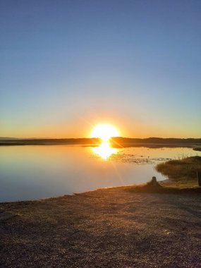Durgun göl yüzeyini aydınlatan parlak bir gündoğumu huzurlu ve huzurlu bir manzara yaratır..