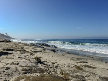 La Jolla San Diego 'da kayalık bir plaj yumuşak kum ve dalgalarla kıyı boyunca aydınlık bir gün ortası gökyüzünün altında.