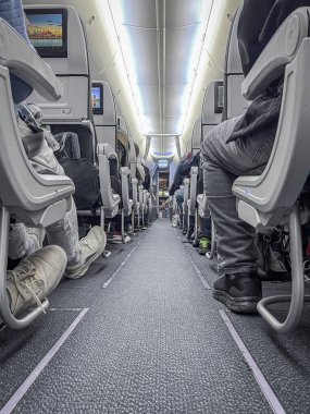 Kabin ışıkları ile aydınlatılmış, kokpite bakan koridor perspektifli yolcuları gösteren uçak kabini manzarası.
