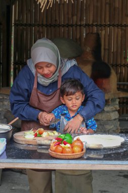 Mutlu aile babası, ebeveyn tesettürlü anne küçük çocuğa fırın yapmayı öğretiyor, küçük tatlı çocuk merdaneyi tutuyor, annesine mutfakta pasta ya da bisküvi yaparken yardım ediyor.