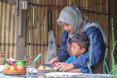 Mutlu aile babası, ebeveyn tesettürlü anne küçük çocuğa fırın yapmayı öğretiyor, küçük tatlı çocuk merdaneyi tutuyor, annesine mutfakta pasta ya da bisküvi yaparken yardım ediyor.