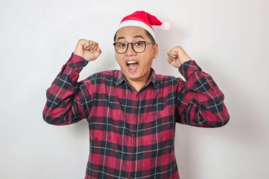 Noel Baba şapkası ve uzun kollu kırmızı ekose gömlek giyen Asyalı genç bir adam bir ödül ya da iyi haber kazanır.