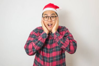 Şaşırmış ve şaşırmış genç Asyalı adam Santa Hat 'ta dans ediyor, alkışlıyor, beyaz arka planda izole edilmiş Noel' i kutluyor.