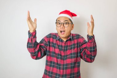 Şaşırmış ve şaşırmış genç Asyalı adam Santa Hat 'ta dans ediyor, alkışlıyor, beyaz arka planda izole edilmiş Noel' i kutluyor.