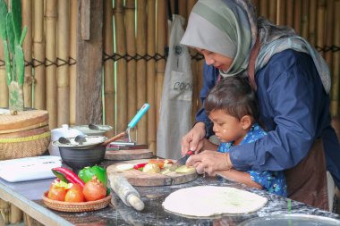 Mutlu aile babası, ebeveyn tesettürlü anne küçük çocuğa fırın yapmayı öğretiyor, küçük tatlı çocuk merdaneyi tutuyor, annesine mutfakta pasta ya da bisküvi yaparken yardım ediyor.