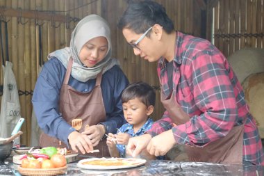 Zevkli meraklı çocuk kızı ev yapımı pizzayı ısırıyor. Anne daighter 'ı elleriyle besliyor. Mutlu baba pizzayı tadıyor. Pizza malzemeleri ahşap masada yemek pişirmek için..