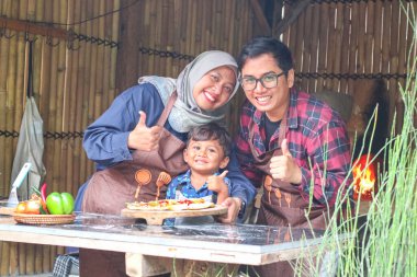 Komik Müslüman aile çocuğu, anne ve baba mutfakta akşam yemeği için pizza yapıyor. Mutlu aile birlikte.