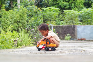 Çocuğun eli kirli zeminde oyuncağıyla oynuyordu. Doğa araştırması, araştırma ve keşif, biyoloji ve botanik alanında bilim ve bilgi. Asyalı çocuklar. Resim