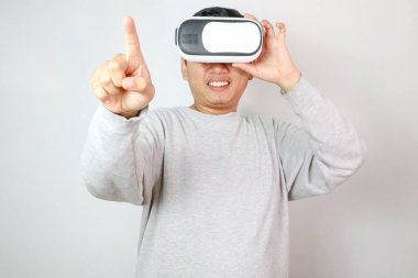 Excited young Asian wearing VR headset with hand pointing to space on web banner grey background. clipart