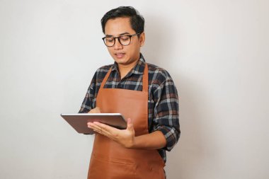 Önlük giyen Asyalı adam tablet, kahve dükkanı ve restoran işletme konseptine bakıyor.