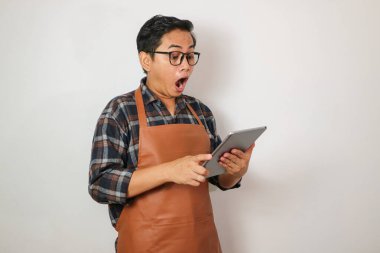 Tablet, kahve ve restoran işletme fikrine bakarken şaşırmış bir ifadeyle önlük giyen Asyalı bir adam.