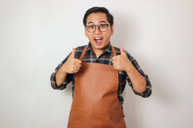 Önlük takan Asyalı adam iki eliyle baş parmak işareti yapıyor.