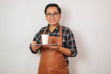 Önlük giymiş Asyalı bir adam kahve servisi yapıyor ve kahve getiriyor.