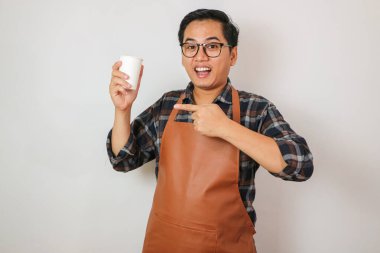 Önlük takan Asyalı adam kahve bardağını işaret ediyor.