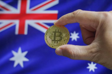 Avustralya bayrağının arka planında elinde altın bir kripto para olan bir adamın eli. Dijital bozuk paralar.