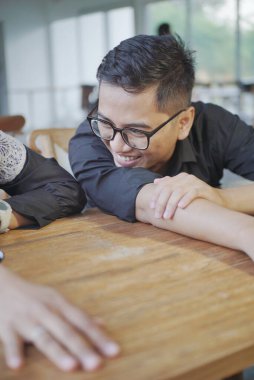 Asyalı bir adam bir kadınla mutlu mesut konuşurken masada yatıyor.