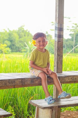 Asyalı çocuklar. 4 yaşında bir çocuk, doğal pirinç tarlası atmosferi olan bankta oturuyor. Bali 'de tatil kavramı.