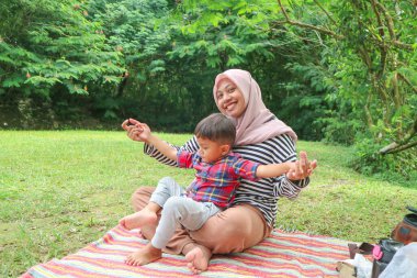 Genç tesettürlü anne, bir yaşında çocuğu var ve parkta oturuyor.