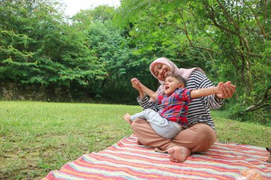 Genç tesettürlü anne, bir yaşında çocuğu var ve parkta oturuyor.