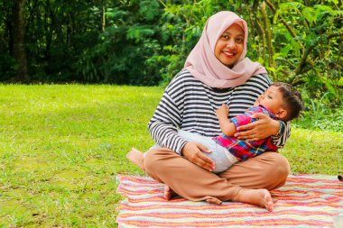 Müslüman bir anne, küçük oğluna güzel gölün yanındaki çimen tarlasında tespih çekerek dua etmeyi öğretiyor. Müslüman aile kavramı.