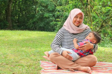 Müslüman bir anne, küçük oğluna güzel gölün yanındaki çimen tarlasında tespih çekerek dua etmeyi öğretiyor. Müslüman aile kavramı.