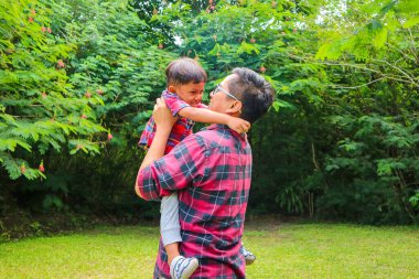 Baba oğlunu bahçede havaya kaldırıyor.